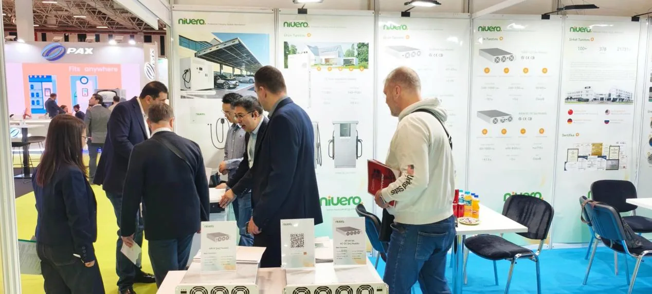 Visitantes e equipe conversando no estande, com módulos de recarga expostos sobre a bancada