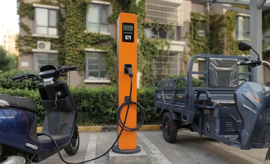 Estação de recarga de pedestal entre uma scooter e um triciclo elétrico de carga, em um estacionamento de condomínio