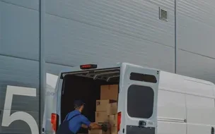 Entregador carregando uma van diante de um galpão logístico