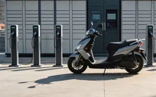 Moto elétrica estacionada diante de um gabinete e de terminais de recarga
